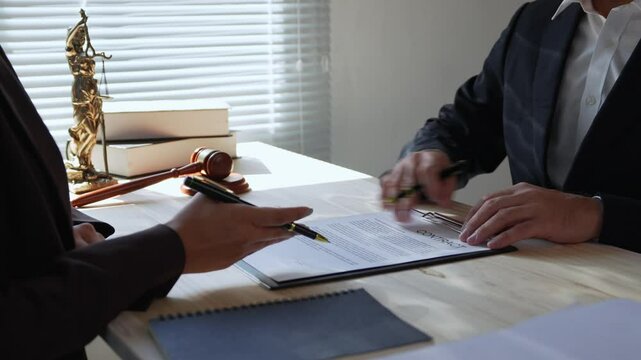 Lawyer explains a contract to a businesswoman, pointing at a specific clause. She holds a pen, preparing to sign the document
