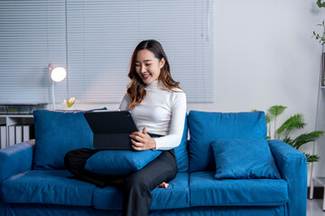 Young asian businesswoman sitting on sofa using tablet computer working at home