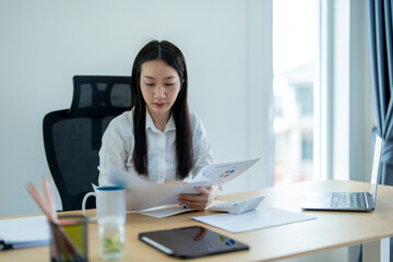 Asian businesswoman reading financial report documents at office desk