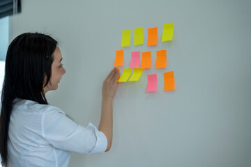 Businesswoman organizing her ideas using sticky notes on white wall