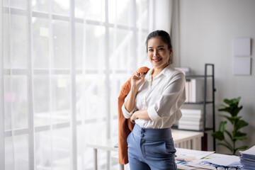 Fototapeta premium Young businesswoman smiling while holding her jacket in a modern office