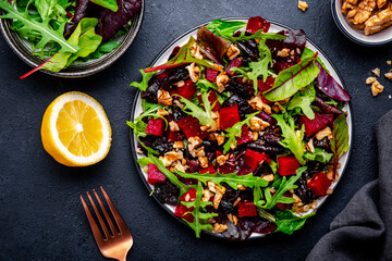 Fresh vegan salad with beetroot, prunes, arugula, chard and walnuts on black background