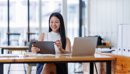 Business asian woman or female worker using a laptop computer to analyse her financial...