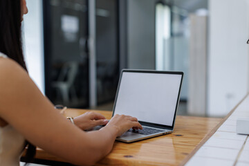 Fototapeta premium Business asian woman or female worker using a laptop computer to analyse her financial data.business people research or financial strategy in company concept. Laptop white screen mockup.