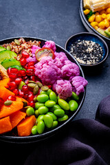 Vegan buddha bowl with vegetables, quinoa, edamame, tofu, quinoa and seeds, black background, top view