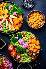 Vegan buddha bowls set for balanced diet with vegetables, quinoa, soybeans, tofu and seeds, black background, top view.