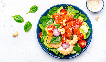 Seafood salad with shrimp, salmon, avocado, spinach, cucumber, tomato, cashew and sesame seeds.. White background, top view