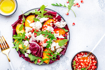Italian salad with arugula, radicchio, peaches, ricotta cheese and pomegranate seeds on white background, top view