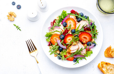 Strawberry and chicken fresh salad with arugula, blueberries, onion and walnuts, white background, top view