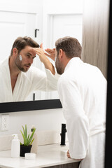 A man is using a cream on his face while standing in front of a bathroom mirror.