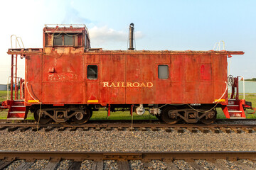 Naklejka premium Rusty Red Rail Car. An old train car sit abandoned on display in a small town. Yellow railroad painted on the sign as it sits idle on the tracks. A historic piece of transport and old time frieght