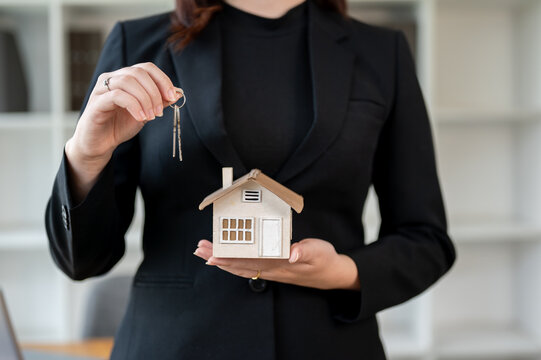 A real estate agent standing in the office, holding house keys and a house model.