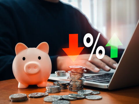 Interest rates, saving account, profit, financial, Investment loans concept. Pink piggy bank and many coin piles on table while man work by laptop computer with percentage increase and decrease icon.