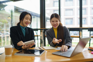 Two young Asian businesswomen discussed investment project work and planning strategy. Business people talk together on laptop computers at the office.
