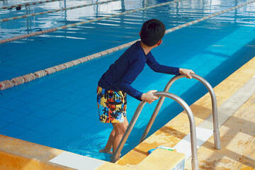 Boy entering swimming pool holding handrail at a sunny indoor pool