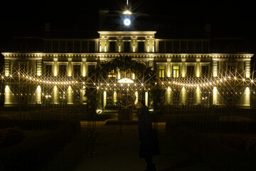 A grand view of Koceni Manor at night, beautifully lit with golden lights that create a starburst...