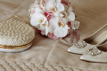 A bouquet of white flowers sits on a bed next to a purse and a bottle of perfume