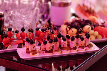 A table with a variety of appetizers and desserts, including fruit skewers and sandwiches. The table is set for a party or gathering, and the food looks delicious and inviting