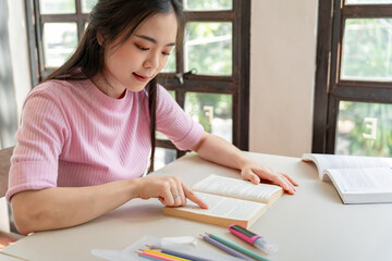 Asian girl student reading book preparing for college exam Young female student studying and writing on notebook making  in school library