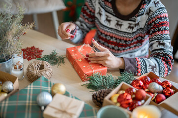 Woman in knitted sweater wrapping christmas presents with eco paper girl packing christmas gifts Xmas holiday concept
