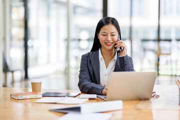 Business Asian woman freelancer is working her job on a laptop computer and phone call in the office. Doing accounting analysis report real estate investment data, Financial and tax systems concept.	