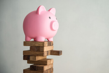 Pink piggy bank on unstable wood tower block game with white wall background copy space. Risk and...