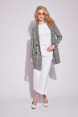 Fashion female model in grey checked coat, white culottes jeans, top, heels shoes, and sunglasses.