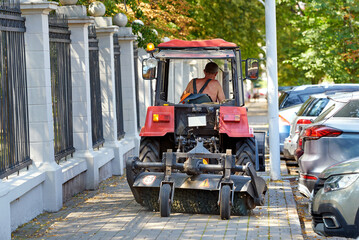 Tractor with rotating brush sweeping city sidewalk. Urban cleanliness in action, city maintenance. Tractor sweep with rotating brush cleaning sidewalks and roads