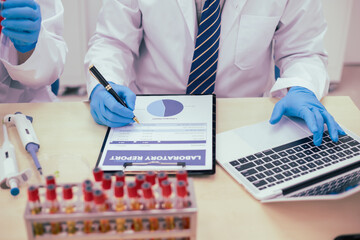 Two male researchers are conducting chemical research in a science lab, carefully analyzing substances at a desk filled with scientific instruments and chemical solutions in a well-organized