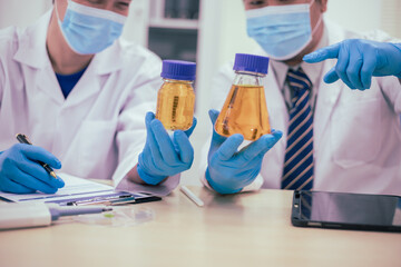 Two male researchers are conducting chemical research in a science lab, carefully analyzing substances at a desk filled with scientific instruments and chemical solutions in a well-organized