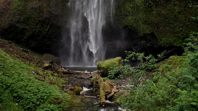 Slow motion landscape still of running waterfall lake Multnomah Falls Columbia river gorge creek bed with mossy rocks plants trees cave Oregon travel tourism USA America