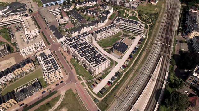Aerial approach of Dutch residential urban development and infrastructure of Noorderhaven neighbourhood in Zutphen, The Netherlands, with rooftops full of solar panels along train tracks.
