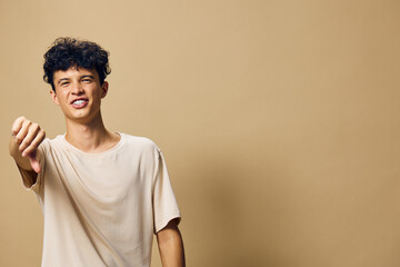 Young man gesturing with a playful expression, set against a beige background The casual t shirt...