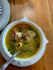 Red Snapper fish spicy soup Sour curry in a white bowl with garlic, tomatoes, vegetable and chili turmeric sauce and various spices, over wooden table. delicious food.