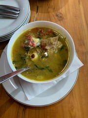 Red Snapper fish spicy soup Sour curry in a white bowl with garlic, tomatoes, vegetable and chili turmeric sauce and various spices, over wooden table. delicious food.