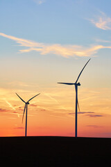 Silhouetted wind turbines in countryside landscape during sunset. Wind power plant generating clean energy. Concept of renewable and sustainable energy