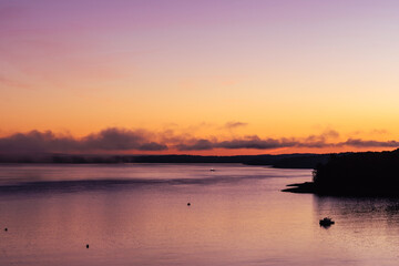 Alpenglow foggy pink and orange sky at sunset consumes the view, reflecting on the bay water,...