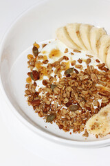 Bowl of Greek Yogurt Served with Granola, Nuts, Seeds, Honey and Banana Slices. 
