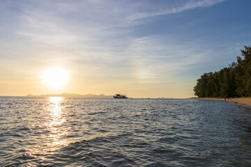 A tranquil beach scene at sunset, highlighting the shimmering water, gentle waves, and lush greenery.