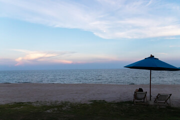 A tranquil beach scene featuring an umbrella and lounge chairs overlooking the serene ocean during a colorful sunset.