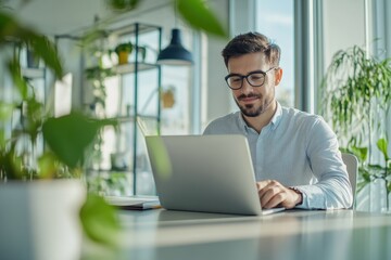 Fototapeta premium High-resolution brightly lit photorealistic candid photograph of a young professional man marketer working on a laptop in a modern office. The photograph is styled like a high-end lifestyle magazine.