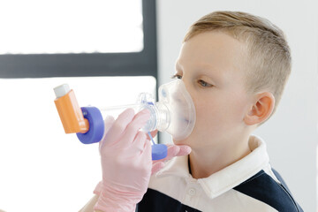 Boy with allergic asthma, inhaling his medication through spacer while sitting in doctors office