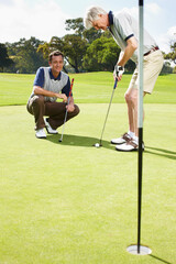 Fototapeta premium Coaching, hole and men on golf course together for teamwork, outdoor fun and fitness competition at club. Sports, senior father and son on green for partnership, bonding and support in healthy hobby.