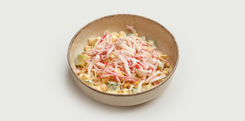 A fresh and colorful crab salad is presented in a beige bowl against a clean white background. The salad is made with a combination of imitation crab meat, corn, avocado, and a creamy dressing. © ismishko