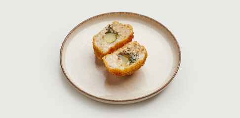 A crispy and golden-brown Kyiv-style chicken cutlet is presented on a beige plate against a clean white background. The cutlet is filled with herb butter and breaded to perfection.