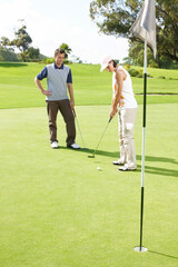 Fototapeta premium Hole, coaching and couple on golf course with club, outdoor fun and fitness on weekend morning together. Ball, woman and man on green grass for outdoor sports, challenge and competition with exercise