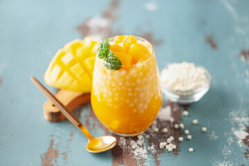 Mango sago creamy dessert in a glass on blue wooden  background