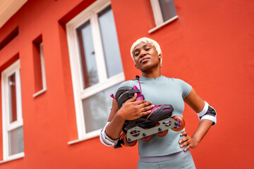 Confident and proud african woman carrying inline skates on shoulders