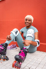 African woman smiling sitting on the ground wearing inline skates