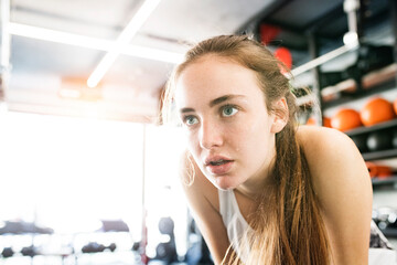 Young fitness girl with sweat on face feeling exhausted after hard workout in gym, holding knees, breathing.